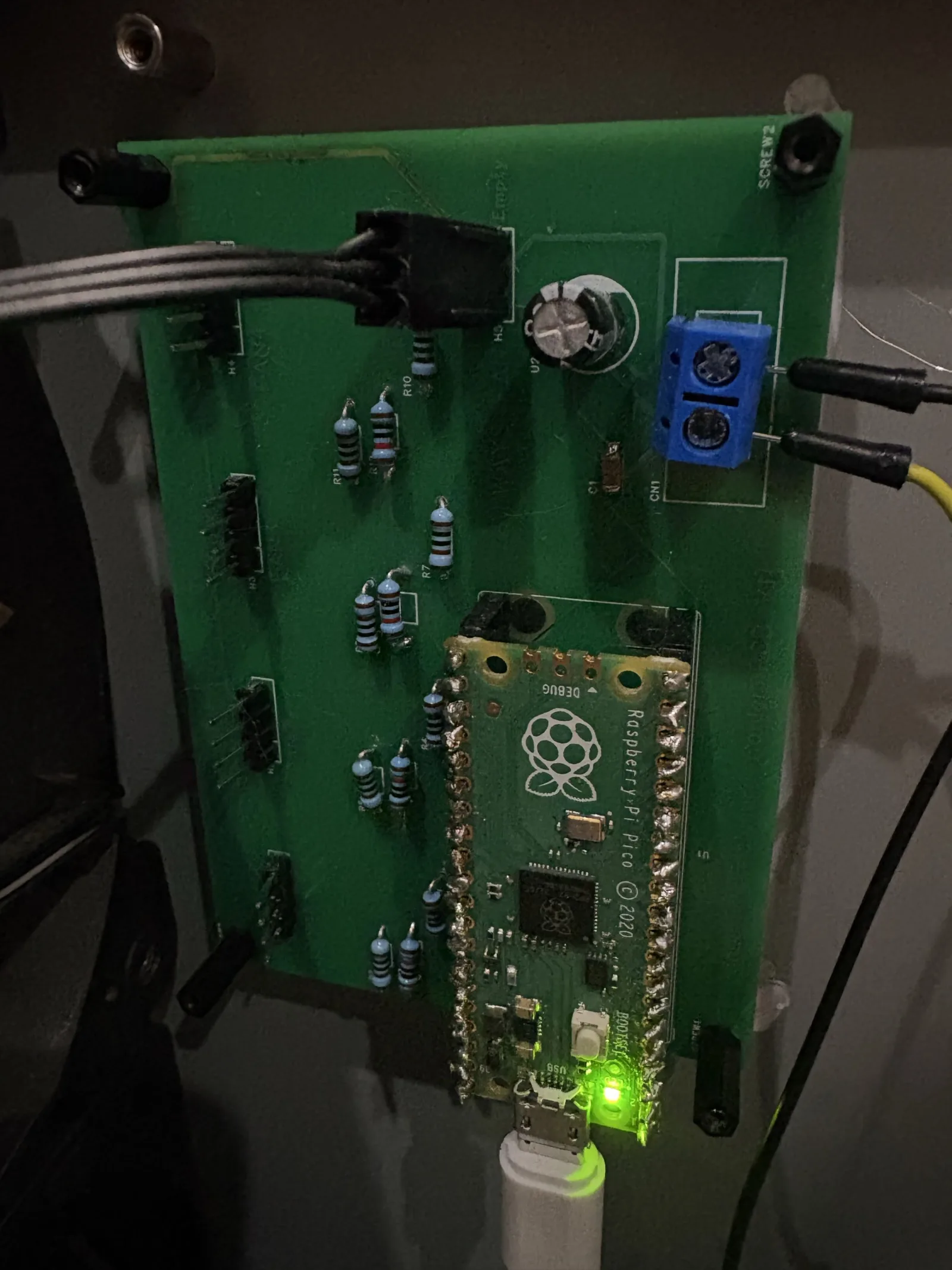 A hand-soldered green PCB with a Raspberry Pi Pico, resistors and a screw terminal, the Pico's LED lit